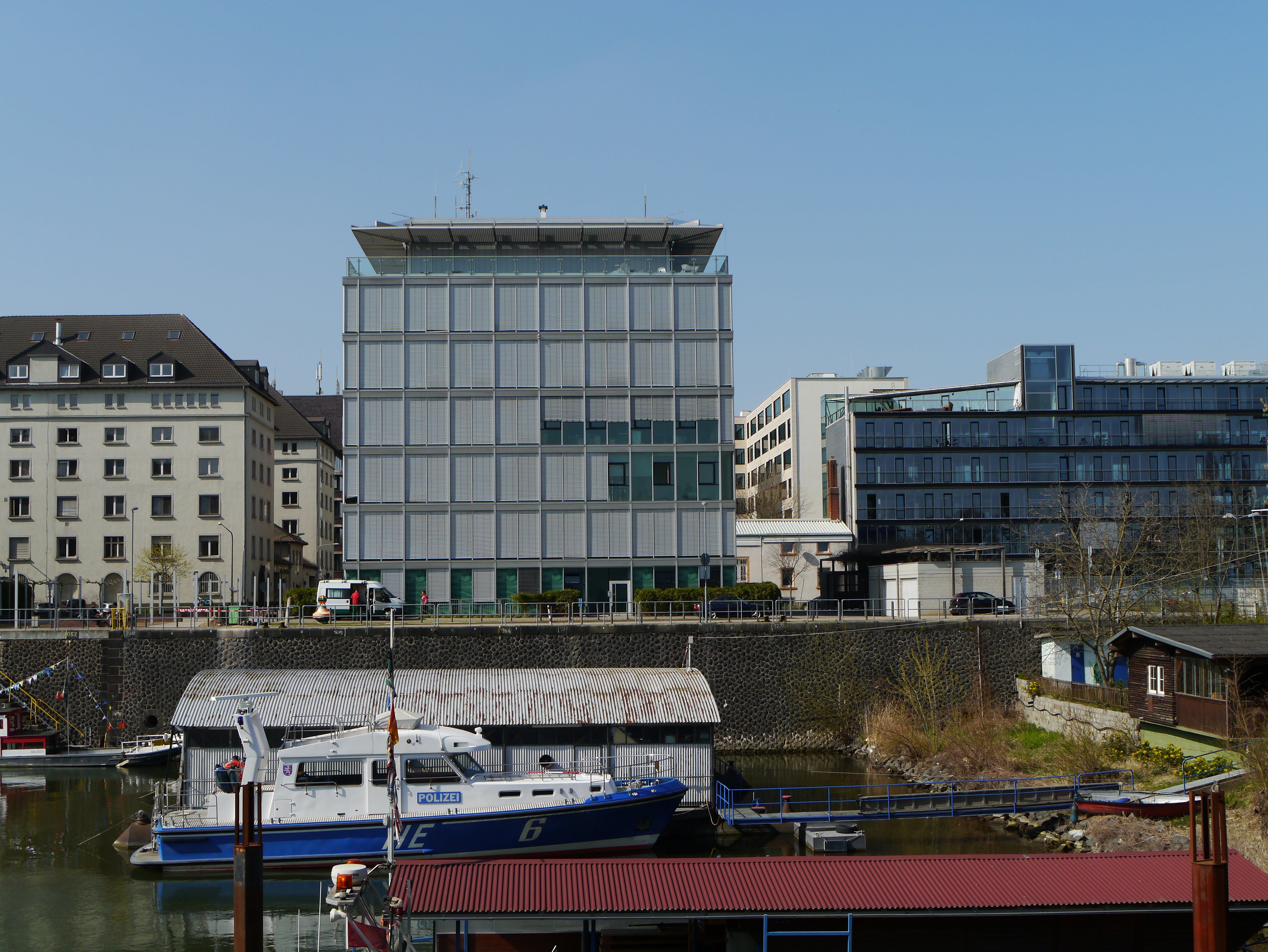 Ein modernes Gebäude mit einer gitterartigen Fassade, das am Osthafenbecken mit Booten liegt.